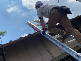 屋根瓦の軒先にハシゴを掛け屋根に登るスタッフ