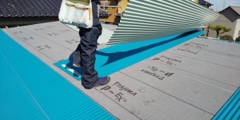 新しい波トタンを施工する為トタンを運ぶ職人