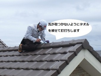 平板瓦屋根の棟部にまたがり棟の釘を打ち込む店長
