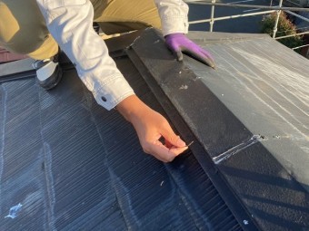 屋根修理を行う為に棟から釘を抜くスタッフ