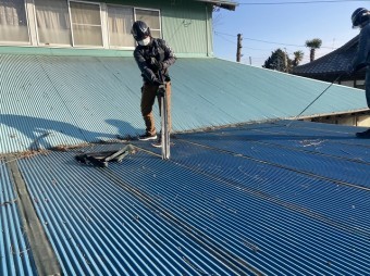 屋根に応急処置された防水テープを剥がす職人