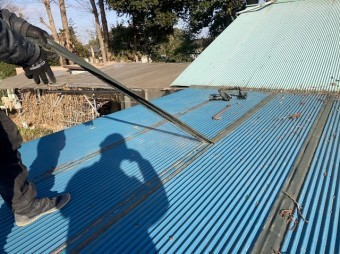 トタン波板に応急処置された防水テープを引っ張り剥がす職人
