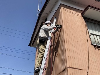 トタン外壁に梯子を掛け、ビスを打ち増しするスタッフ