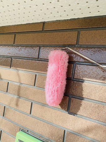 高意匠サイディングにUVクリアー塗装をピンク色のローラーで塗布