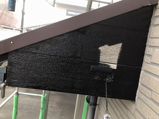 ローラーで木製破風板に黒い塗料を塗布