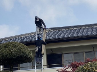 職人が梯子で荷上げた荷物を受け渡す様子