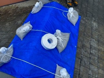 雨漏り部をブルーシートで養生し土嚢をロープでくくる