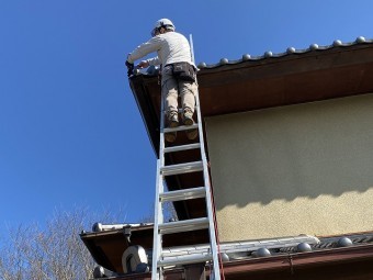 二連梯子を架け、雨樋の撤去作業を行うスタッフ