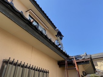 下屋根に脚立を掛け作業する職人