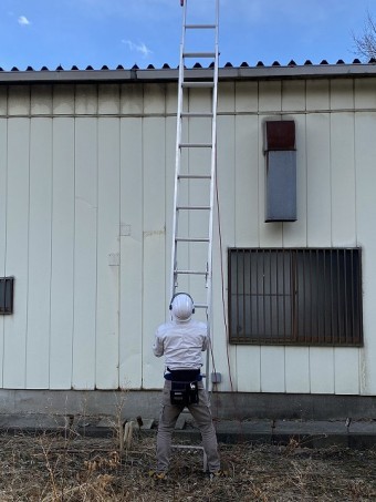 折板屋根に二連梯子を掛けるスタッフ