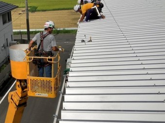 高所作業車に乗った職人と屋根上にいる職人が連携して雨樋交換作業