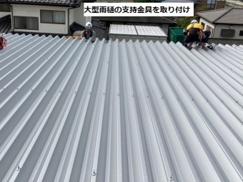 大きな折板屋根の軒先に雨どい支持金具を取り付ける作業員