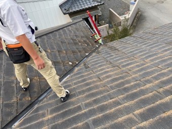 スレート屋根の谷部にまたがり仁王立ちするスタッフ