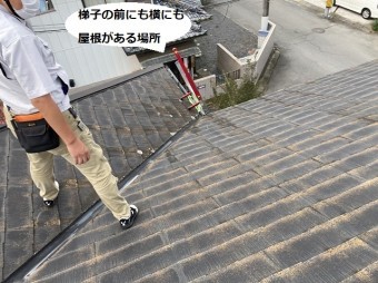 梯子から屋根に登り谷樋にまたがって立つスタッフ