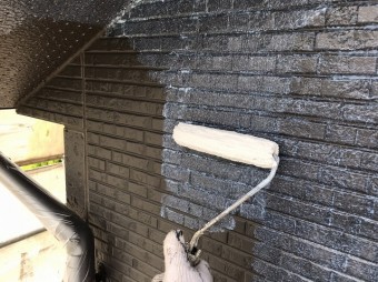 こげ茶色のサイディングに下塗り材をローラーで塗布する