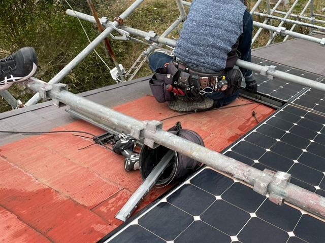 屋根足場で体を支えながら太陽光パネルを撤去する作業員