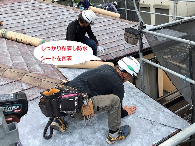 ひたちなか市で施工中の屋根へ粘着式防水紙シートを押さえつけ密着させる