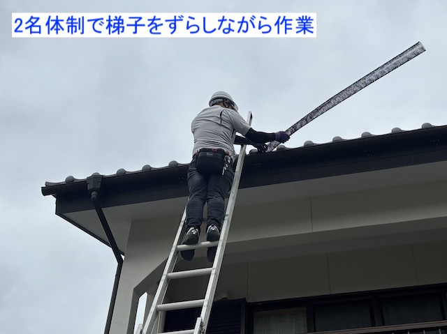梯子にのり、雨樋ネットを設置するスタッフ