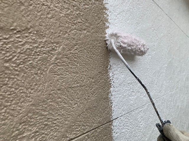 ベージュの外壁に白い下塗り塗料を塗布