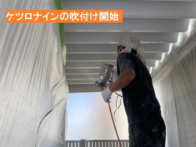 車庫の折板屋根の裏地に吹付塗装を行う職人