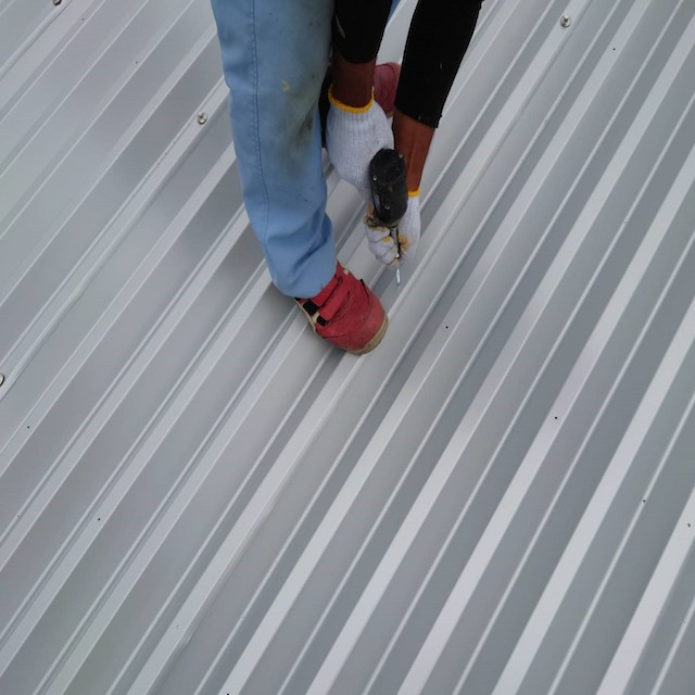 折板屋根にボルト止めを行っている職人