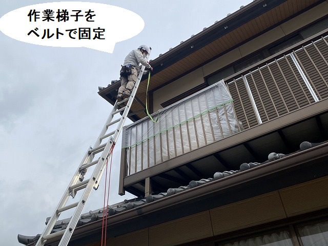 作業用の梯子を軒先に掛け、ベルトで固定するスタッフ